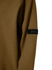 Brown ribbed long sleeve shirt with black patch featuring partial text on the upper arm against a white background.