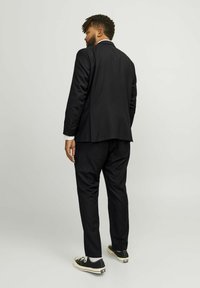 Schwarzer Anzug mit einem Einlass-Jackett und passender Hose, kombiniert mit schwarzen Sneakers. Glatter Stoff mit taillierter Passform.