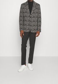 Blazer a motif bianco e nero con una vestibilità su misura, indossato sopra un dolcevita nero, abbinato a pantaloni neri e sneakers bianche.