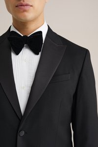 Črn smoking s satenskimi reverji, bela srajca z naborki in črn žametni metuljček. Ozek kroj z enim gumbom za zapiranje.