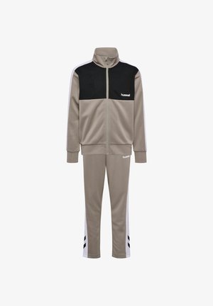 Dreng iført gråt og sort træningssæt med hvid side striber og matchende sneakers, står og kigger til venstre.