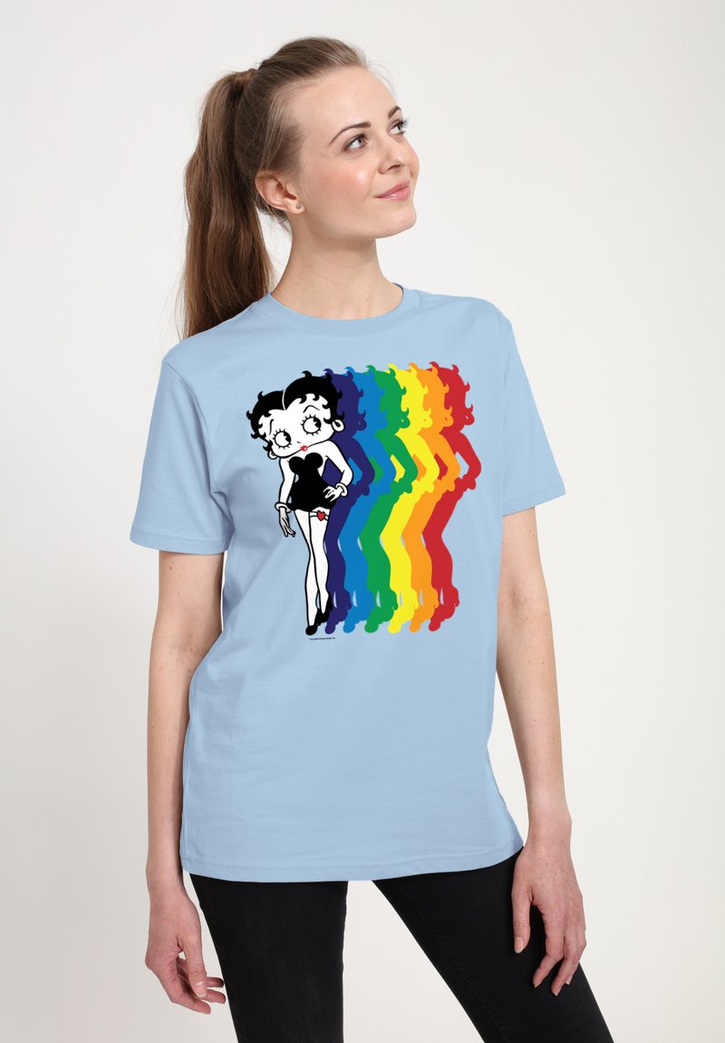 T-shirt bleu clair avec un personnage de dessin animé en noir et blanc, sur fond de silhouettes aux couleurs de l'arc-en-ciel. Manches courtes, coupe décontractée.