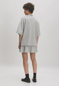 Grijze oversized sweater komt iets over een uitlopende grijze rok, met korte mouwen, ronde hals, en gecombineerd met zwarte schoenen en sokken.