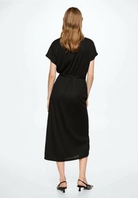 Abito midi nero a coste con maniche corte, vita sormontata da una cintura e texture sottile. Caratterizzato da una vestibilità ampia, arriva poco sopra le caviglie.