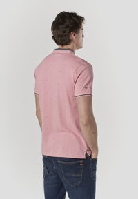 Roosa polo-särk tekstuurse mustriga, lühikeste varrukatega ja tumesiniste kaeluse ning varrukaservade detailidega, kombineeritud tumedate teksapükstega.