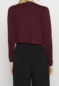 Burgundowa krótka bluzka z długim rękawem, wykonana z miękkiego materiału, o prostym wzorze i prostym wykończeniu, zestawiona z czarnymi spodniami o wysokim stanie.