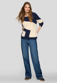 Marineblauer und cremefarbener Pullover mit Farbblock-Design, aus weichem Material, mit lockerem Schnitt und rundem Ausschnitt, kombiniert mit hellen, ausgestellten Jeans aus Denim.