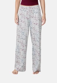 Femme portant un pantalon de pyjama gris clair avec des dessins de nounours bleus et bordeaux et une taille à boutons, pieds nus.