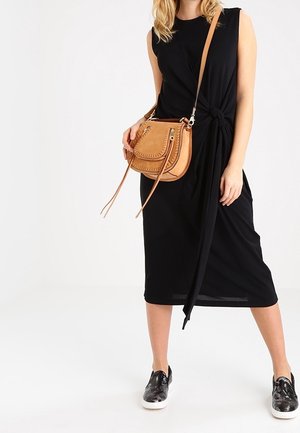 Schwarzes Midi-Kleid mit Knotendetail, kombiniert mit einer tan-farbenen Ledertasche über der Schulter mit Nahtdetails und hellen Sneakers.