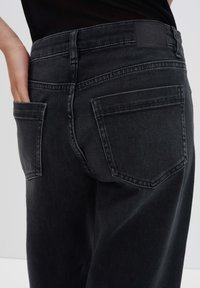 Jeans in denim neri con un taglio dritto, dotati di due tasche posteriori e una texture liscia. La cintura presenta una toppa in pelle rettangolare.