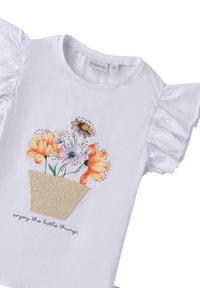 Camiseta blanca con mangas con volantes, que presenta un estampado colorido de una flor en una maceta y el texto "disfruta de las pequeñas cosas" debajo del diseño.