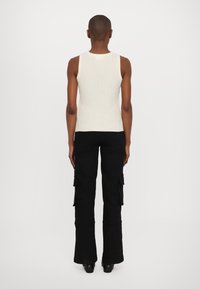 Top sin mangas blanco acanalado y pantalones cargo negros con piernas acampanadas. Los pantalones cargo cuentan con bolsillos laterales y una tela texturizada, vistos desde la parte trasera.