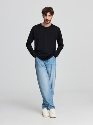 Maglietta nera a maniche lunghe abbinata a jeans larghi azzurri e sneakers bianche. Design semplice, tessuto morbido e vestibilità comoda.