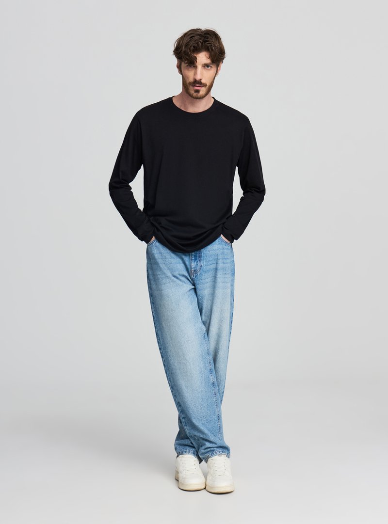 Maglietta nera a maniche lunghe abbinata a jeans larghi azzurri e sneakers bianche. Design semplice, tessuto morbido e vestibilità comoda.