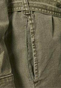 Olivově zelená tkanina s texturovaným povrchem, s boční kapsou a viditelnými švy. Násypkový design v oblasti pasu.