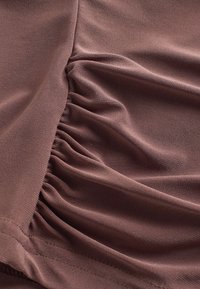 Textured brown fabric featuring gathers along one edge, creating a draped effect. Smooth surface with a slight sheen.