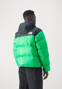 Zeleni puffer jakna s crnim akcentima i kapuljačom, sa kviltanim dizajnom i vidljivim logotipom na ramenu, nošena naopačke.