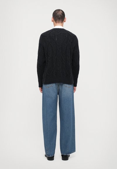 Black cable-knit sweater with a textured pattern, worn with loose blue denim jeans. The outfit features a relaxed fit and simple design.