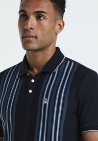 Marineblauwe polo met verticale strepen in lichtblauw en donkerblauw, drie-knopssluiting en een klein logo op de borst.