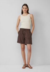 Tan tanktop en bruine shorts. De shorts hebben een elastische tailleband, twee zijzakken en opgerolde mouwen. Sandalen met dunne bandjes maken de outfit compleet.