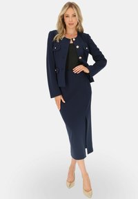 Granatowy, dwuczęściowy zestaw składający się z dopasowanej marynarki z złotymi guzikami oraz midi spódnicy z rozcięciem, zestawiony z cielistymi szpilkami.