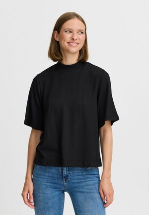 Schwarzes, geribbeltes T-Shirt mit kurzen Ärmeln und hohem Kragen, das einen entspannten Schnitt bietet. Kombiniert mit blauen Jeans, die seinen vielseitigen Stil hervorheben.