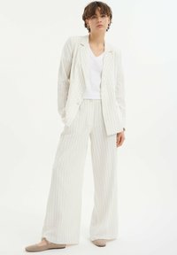 Lichtgekleurde gestreepte pak met wijde broekspijpen en een dubbelzijdig colbert, gecombineerd met een effen witte V-hals shirt en platte schoenen.