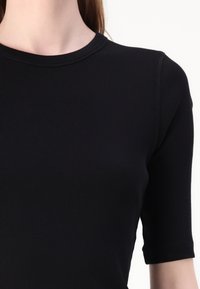 Sort ribbet kortærmet top med rund halsudskæring, der har et tætsiddende design og subtil tekstur. Sømdetaljer ved skuldrene.