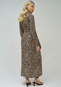 Abito lungo con un motivo animalier a macchie beige e nere, con maniche lunghe e vita legata. Indossato con sandali neri con lacci.