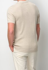 Polo de punto de manga corta color beige con textura de canalé vertical y cuello plano. Se lleva con pantalones de color claro.