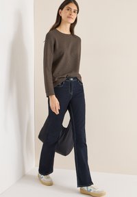 Brown textured long-sleeve sweater, dark blue flared jeans, white sneakers with light blue accents, and a black bag with a cut-out handle.