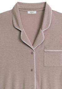 Beżowa piżama z miękkiej tkaniny, z kołnierzykiem z wycięciem, białymi lamówkami, zapięciem na guziki i kieszonką na piersi. Widoczna metka marki "ATLANTIC".