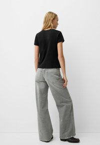 Tricou negru cu mânecă scurtă, asortat cu blugi gri lejeri. Materialul pare neted, iar blugii au un finisaj decolorat, cu buzunare pe spate.