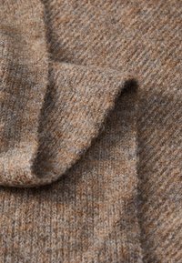 Brun strikket stoff med en teksturert overflate, som har varierende nyanser av beige og lys brun i et mykt, varmt materiale.