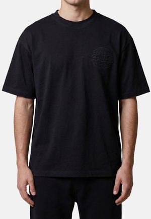 Hombre que lleva una camiseta negra de manga corta con un pequeño globo en relieve y el logotipo "4US" en el pecho izquierdo.