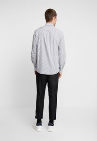 Camicia a righe con maniche lunghe, azzurro chiaro e bianco, con una piega sul retro; abbinata a pantaloni scuri su misura e sneaker bianche.
