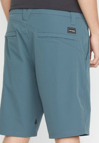 Shorts pour hommes de longueur genou en tissu teal uni. Les caractéristiques comprennent plusieurs poches, une petite étiquette logo et des détails de couture contrastants.
