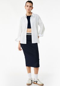 Witte button-up shirt, marineblauw crop top, marineblauwe pencil skirt met witte streep, witte sokken en beige sneakers. Gladde stof, relaxte pasvorm.