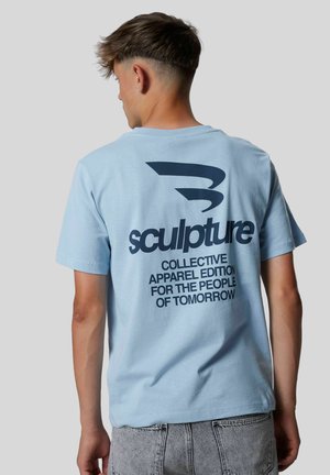 Camiseta de algodón de color azul claro con un gran diseño de texto negro en la parte posterior: "escultura COLECTIVO ROPA EDICIÓN PARA LA GENTE DEL MAÑANA."