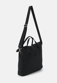 Zwarte nylon draagtas met verstelbare band, dubbele handvatten en versterkte stiksels. Heeft een eenvoudige rechthoekige vorm en een matte afwerking.