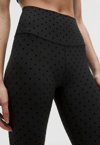 Czarne legginsy z wysokim stanem, z teksturowanym wzorem wypukłych kropek, o gładkim wykończeniu i minimalnych detalach szwów.