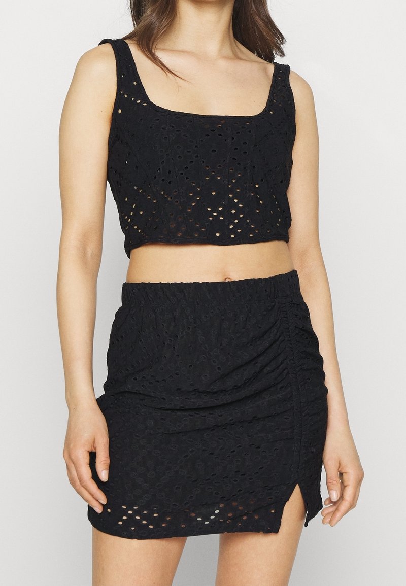 Ensemble noir à deux pièces comprenant un top court avec décolleté carré et une mini-jupe avec texture froncée et fente sur le côté.