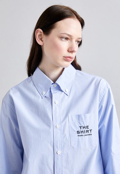 Cămașă cu dungi albastre și albe, cu guler întins, având o buzunar pe pieptul stâng brodat cu "THE SHIRT MARC JACOBS."
