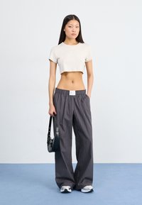 Camiseta corta de un beige claro, combinada con pantalones de pierna ancha a rayas gris. La modelo lleva un pequeño bolso negro de hombro. Zapatillas con acentos claros.