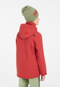 Giacca rossa per bambini con cappuccio e polsini elasticizzati, caratterizzata da un logo sulla schiena. Abbinata a un berretto verde con la scritta "PR."