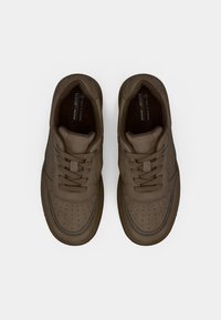 Καφέ vegan αθλητικά παπούτσια με διάτρητο σχεδιασμό στη μύτη, επίπεδα κορδόνια, επενδεδυμένο κολάρο και αντιθετικές ραφές. Μινιμαλιστικό στυλ και λεία υφή.