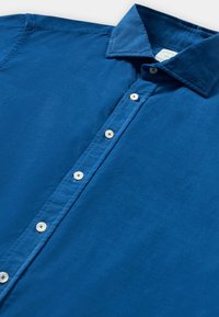 Blauwe corduroy overhemd met knopen en een klassieke kraag, plat gelegd op een witte ondergrond.