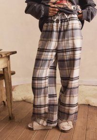 Person wearing gray and beige plaid wide-leg pants with a drawstring waist and fuzzy slippers standing on wooden floor.