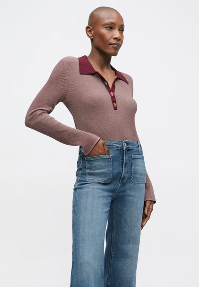 Μακρυμάνικος πλεκτός σκούφος σε μωβ απόχρωση με μπορντό στις λεπτομέρειες του γιακά και κουμπιά, σε συνδυασμό με ανοιχτό μπλε παντελόνι σε ίσια γραμμή.