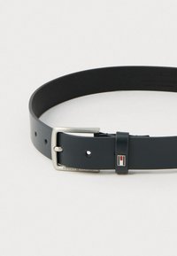 Must mustrihmeline nahkrihm, millel on hõbedane metallist pandla, reguleeritavad augud ja väike värviline logo pandla lähedal. Sile, mati tekstuuriga.